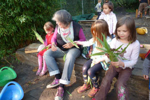 Kinder sitzen im Garten und entfernen güne Blätter von Maiskolben